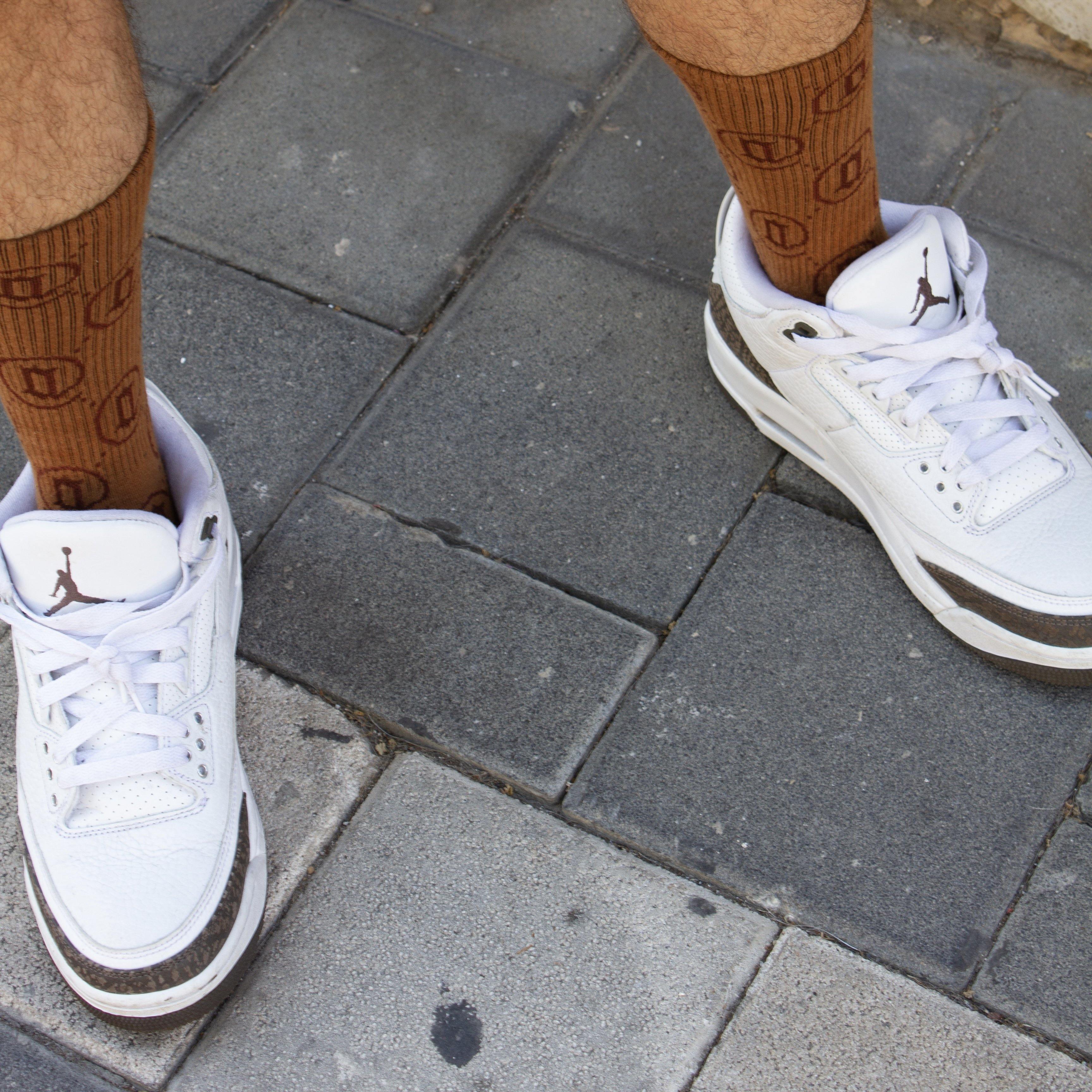 Brown monogram pattern socks paired with white athletic sneakers on pavement