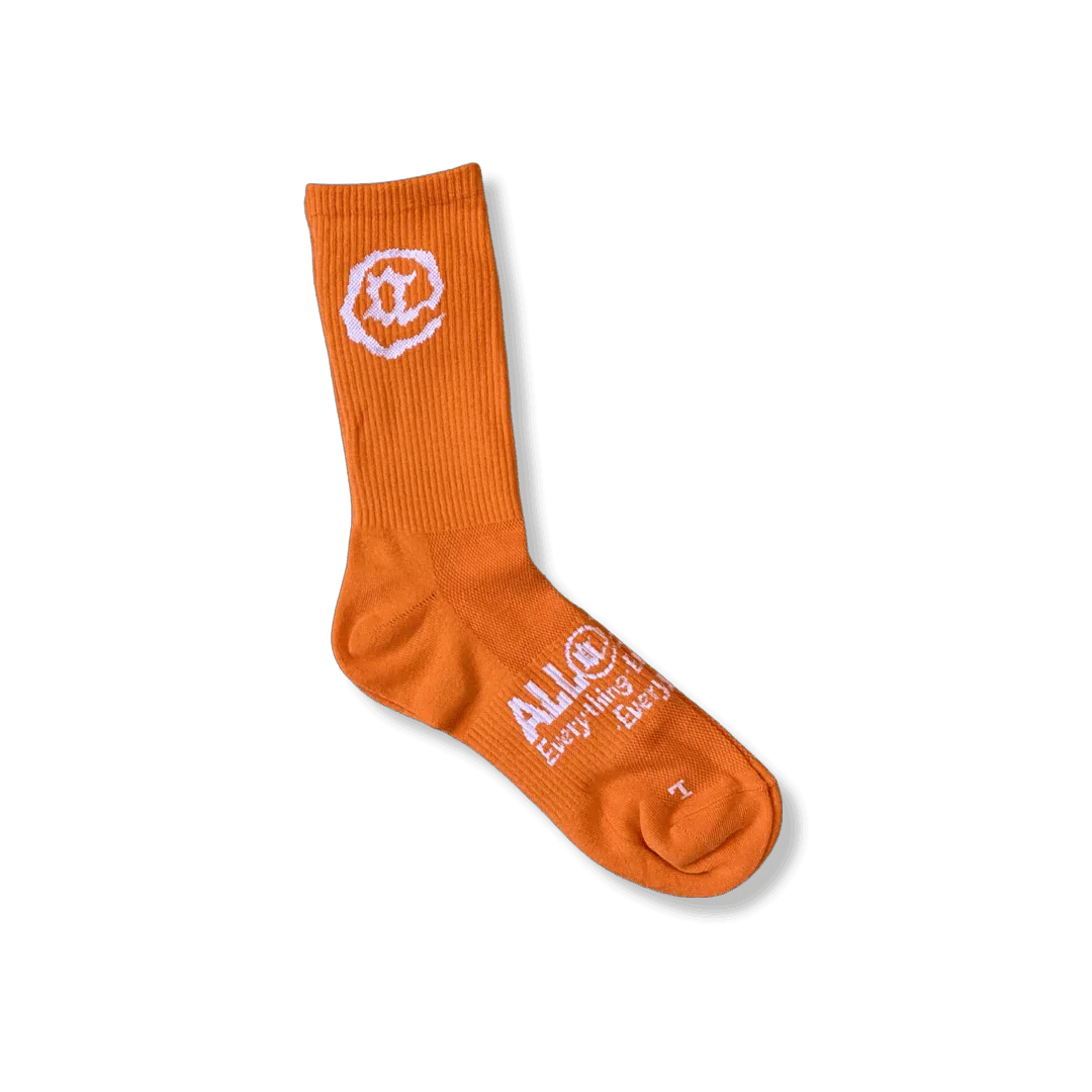 Orange crew sock with white logo and text, ribbed top, isolated on gray background