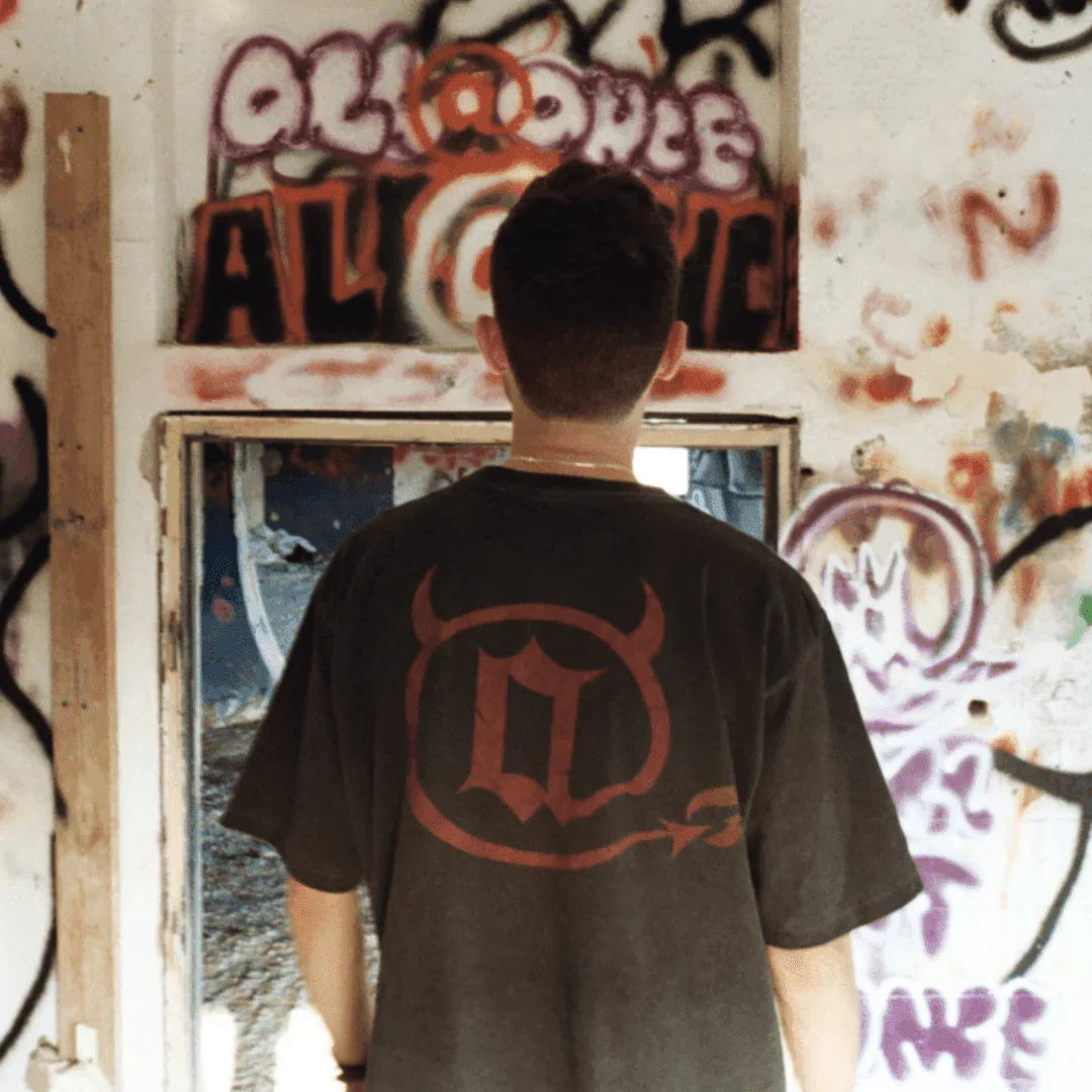 Man in black graphic devil tee stands in front of colorful graffiti wall