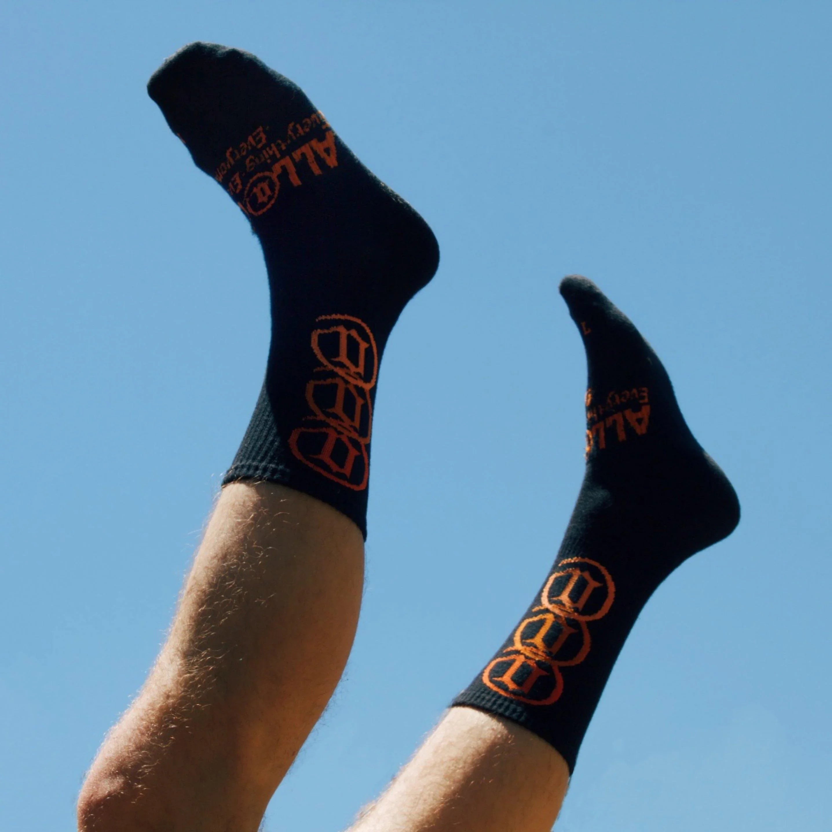 Person wearing black socks with orange graphic and text, legs raised against blue sky