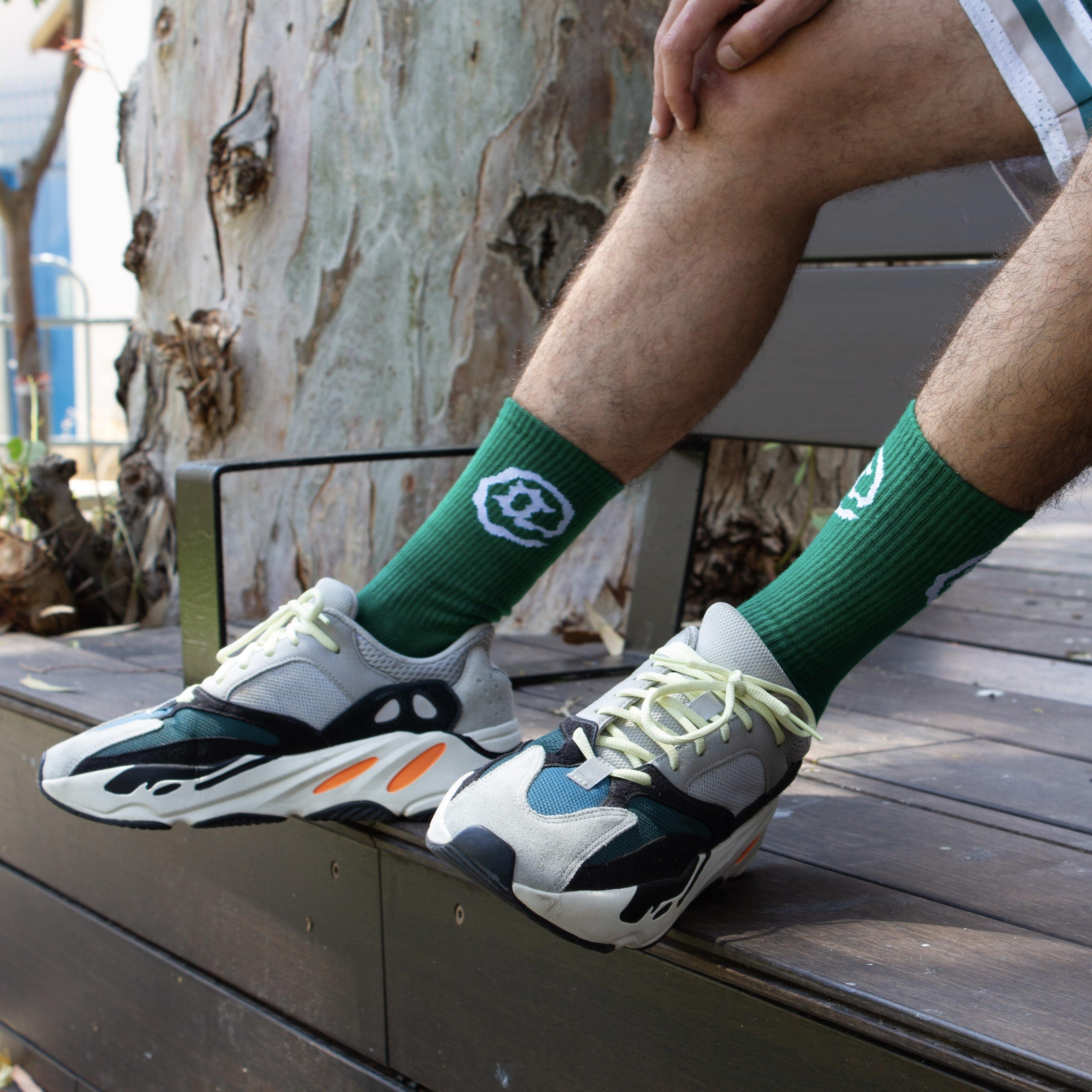 Green socks with white pea pod graphic, worn with sneakers, outdoor bench setting