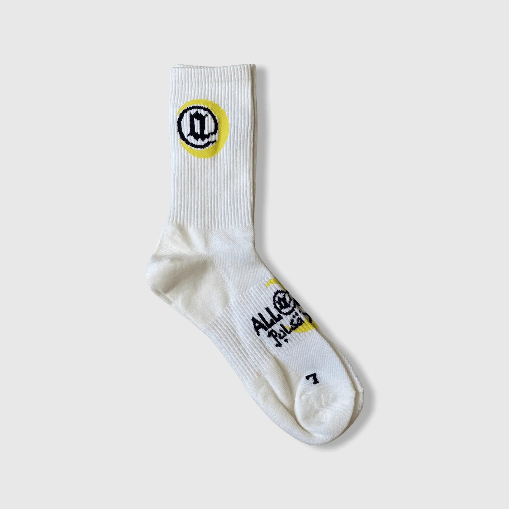 White crew sock with yellow and black circular emblem and printed text, laid flat on gray background