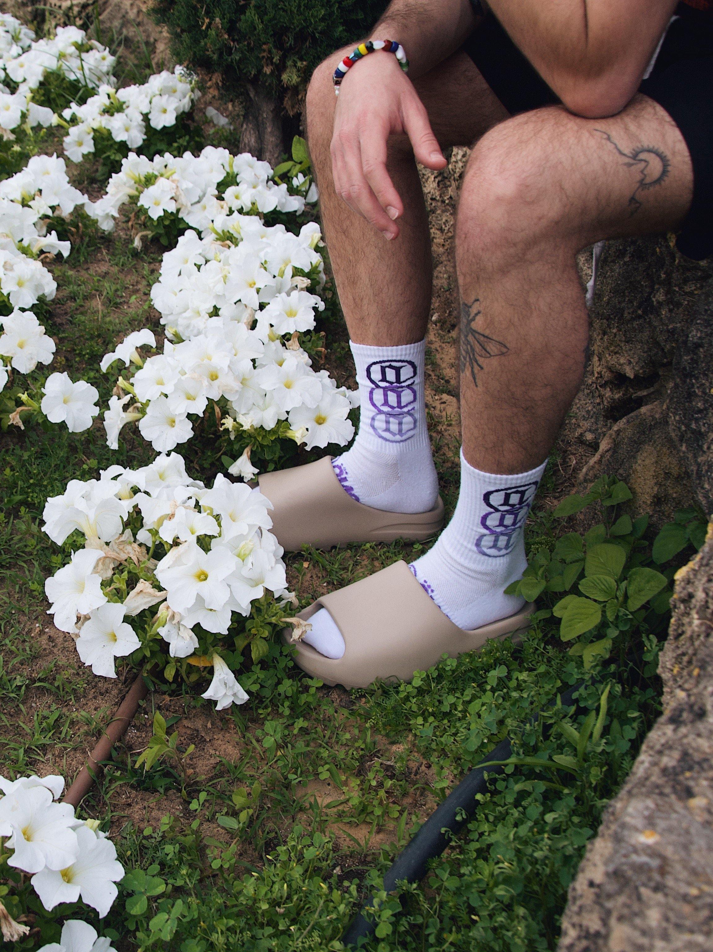 White graphic socks and beige slides worn outdoors near white flowers