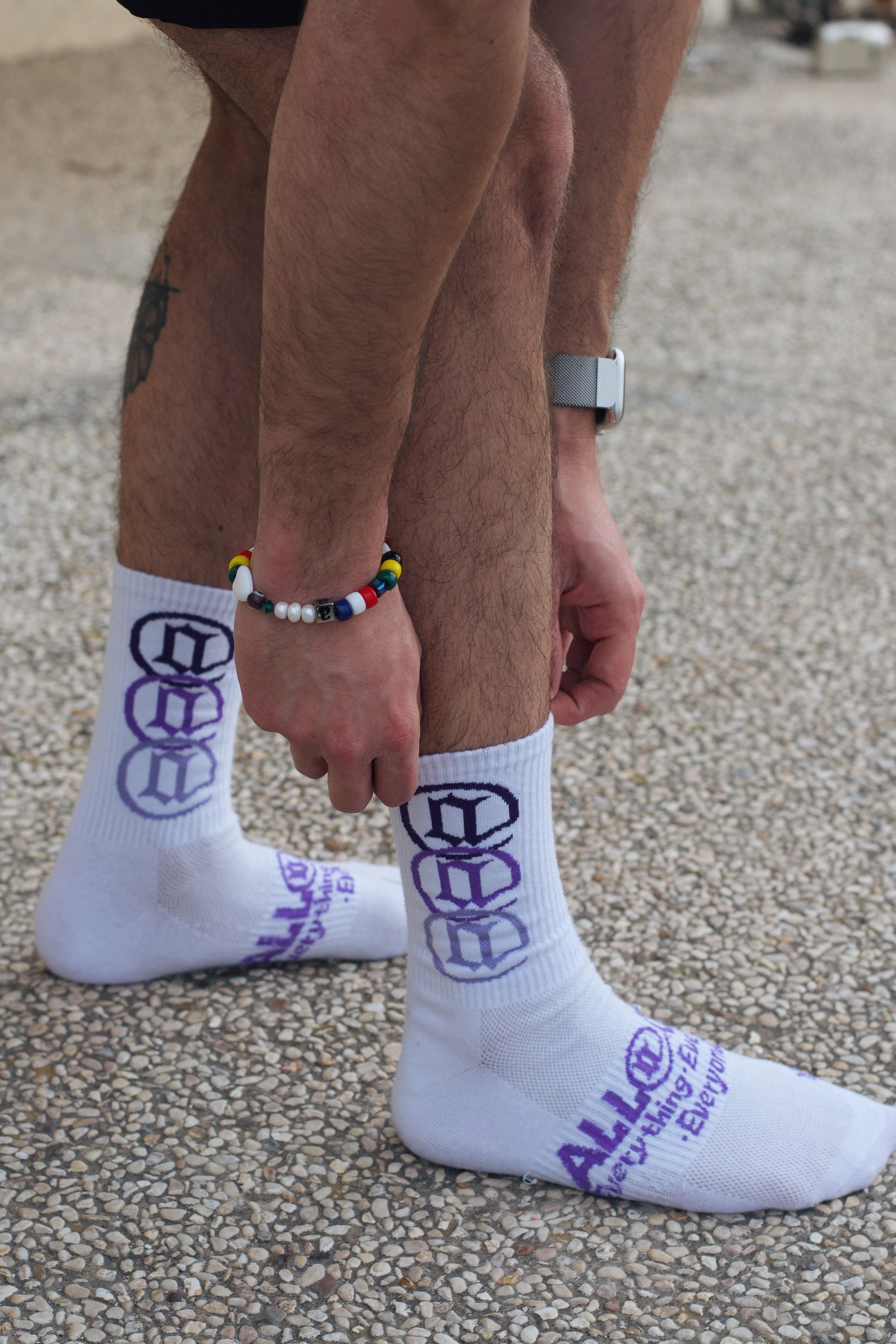 Person wearing white socks with purple graphics and text, standing on a pebble surface